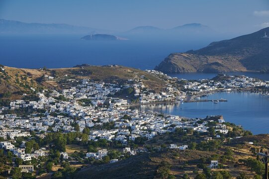 White painted houses of a coastal town, embedded in hilly landscape, surrounded by blue sea, Skala, Patmos, Dodecanese, Greek Islands, Greece