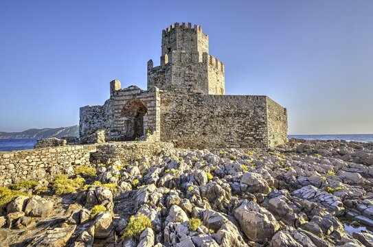 Sunlit castle ruins on a rocky cliff above the sea, octagonal medieval tower. Islet of Bourtzi, sea fortress of Methoni, Peloponnese, Greece
