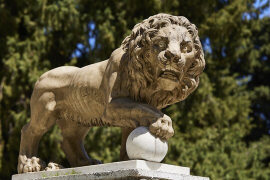 A stone lion statue holding a ball with a forest in the background, Rodini Park, Municipal Park, Rhodes Town, Rhodes, Dodecanese, Greek Islands, Greece