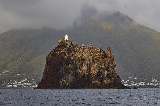 Stromboli island with offshore islet Strombolicchio, lonely lighthouse on rocky island in front of dramatic volcano and cloud veil, UNESCO World Heritage Site, Aeolian Islands, Aeolian Islands, Sicily, Italy