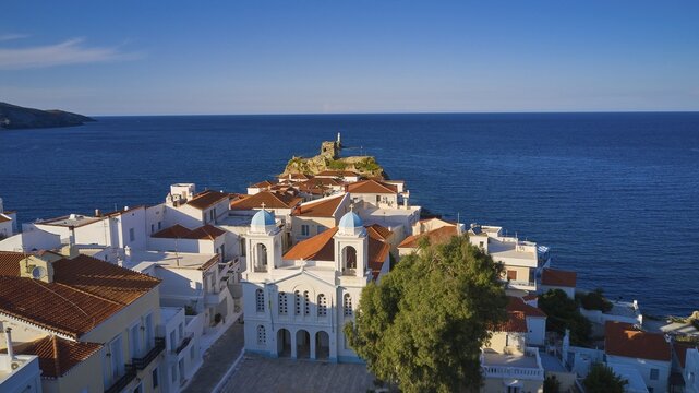 Chora, old town, red tiled roofs, lighthouse, fortress islet, fortress ruins, church, drone shot, evening light, soft evening light, sea blue, Andros town, Andros island, Cyclades, Greece
