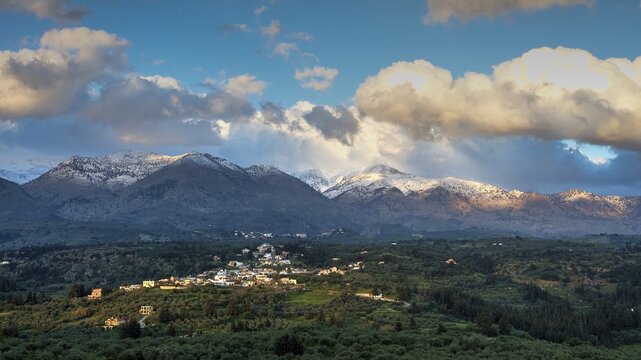 White mountains in morning light, Lefka Ori, snow-capped mountains, village, olive groves, cloudy blue sky, Chania province, Crete, Greece