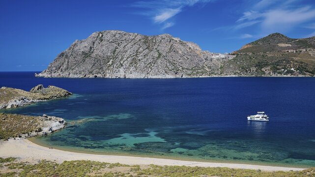 Clear turquoise water with a boat and mountains in the background under a blue sky, Psili Ammos beach, Patmos, Dodecanese, Greek Islands, Greece