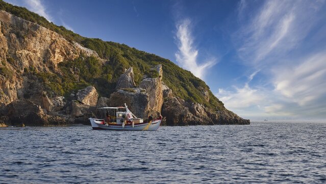 A boat moves along the coast with distinctive cliffs under a sky full of dramatic clouds, morning light, Navarino Bay, Pylos, Peloponnese, Greece