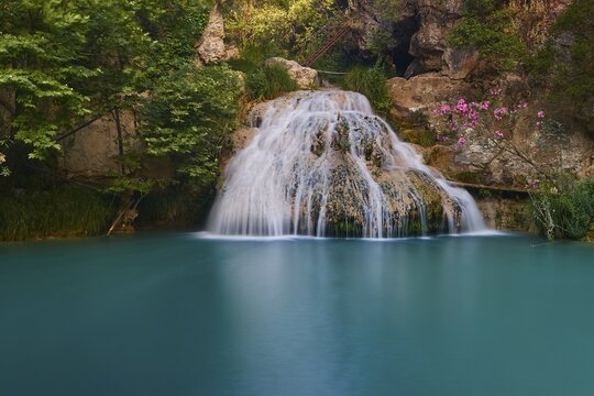 A small waterfall flows into a calm turquoise blue pool, surrounded by flowers and rocks, waterfalls, ponds, Polylimnio, Peloponnese, Greece