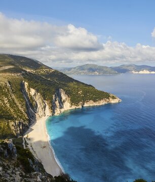 Myrtos Beach, view from above, white sandy beach, bay in cliff, overgrown slopes, blue and turquoise sea, blue sky with grey-white clouds, Kefalonia Island, Ionian Islands, Greece