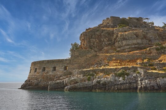 Stone wall in rocky coastal scene by the sea with clear blue sky and calm water, Venetian Sea Fortress, Leper Island, Spinalonga, Elounda Bay, Mirabello Bay, East Crete, Crete, Greek Islands, Greece