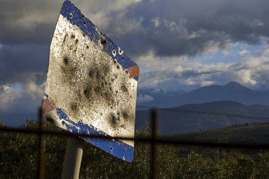 A rusty, tattered road sign in front of a mountainous landscape under a cloudy sky, Lefka Ori, White Mountains, mountain massif, west, Crete, Greece