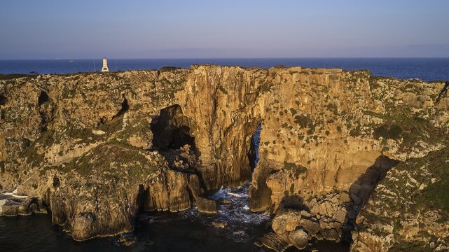 Drone shot, dramatic cliffs with lighthouse and sea in the background in daylight, morning light, Tsichli Babas islet, Sfaktiria island, Navarino Bay, Pylos, Peloponnese, Greece