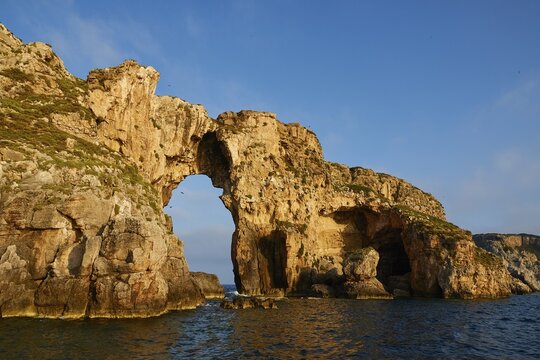 An impressive rock arch rises from the sea, morning light, Tsichli Babas islet, Navarino Bay, Pylos, Peloponnese, Greece