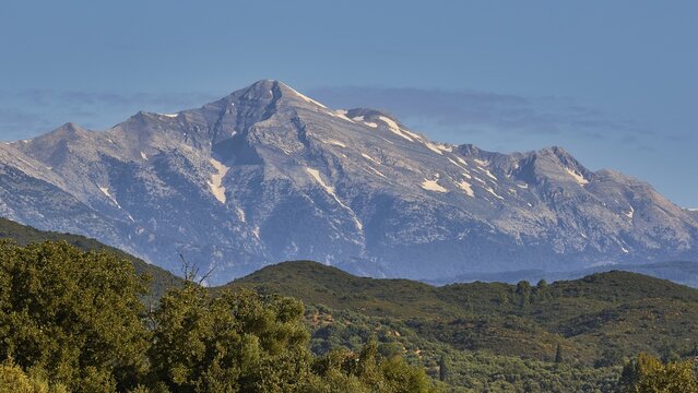 A majestic, snow-capped mountain peak rises above green forests, Taygetos Mountains, Mani Peninsula, Peloponnese, Greece