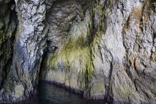 Entrance to a dark cave with irregular rock structures, boat trip around the island of Ortigia, Isola di Ortigia, Syracuse, Sicily, Italy