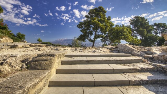 Stone staircase in sunny landscape with trees and mountains in the background under blue sky, UNESCO World Heritage Site, Minoan Palace of Festos, Crete, Greece