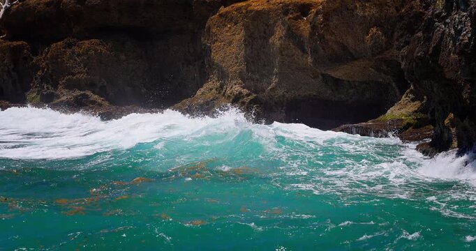 Turquoise ocean waves crashing over rocky coastline with sea foam on a sunny day