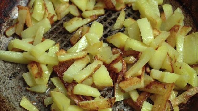 Sliced potatoes being stirred in a frying pan with a wooden spatula, showcasing the cooking process of golden-brown potato pieces in a kitchen setting