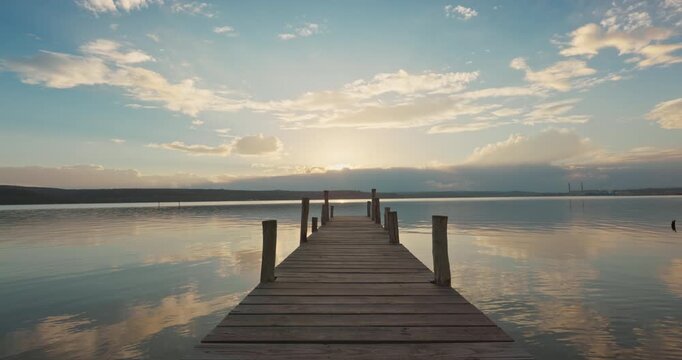 Scenic sunset over the sea, wooden jetty pier on calm lake with clouds reflection at the water surface
