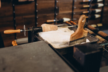Fresh traditional trdelnik is being prepared and rolled in sugar at a street bakery in Prague, Czech Republic. The sweet chimney cake is baked on a rotating cylinder over an open flame, creating a gol © Евгения Жигалкина