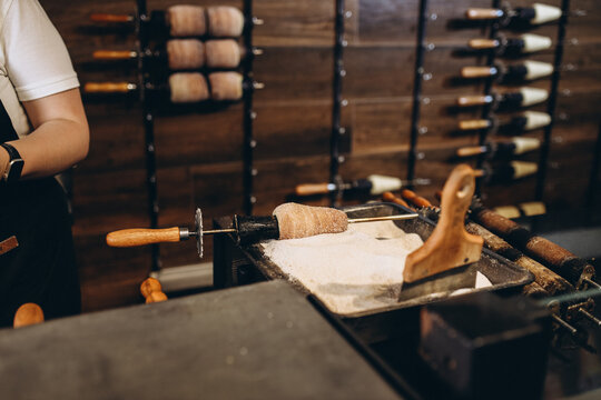Fresh traditional trdelnik is being prepared and rolled in sugar at a street bakery in Prague, Czech Republic. The sweet chimney cake is baked on a rotating cylinder over an open flame, creating a gol