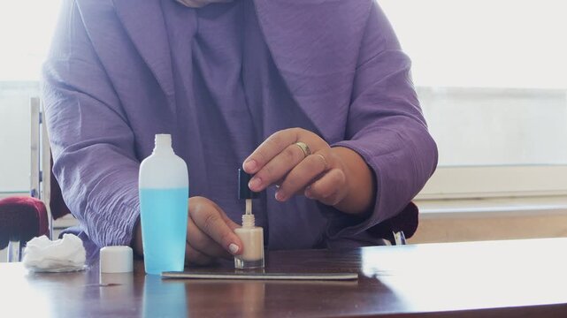 A woman gets a manicure and paints her nails with light polish at a table.