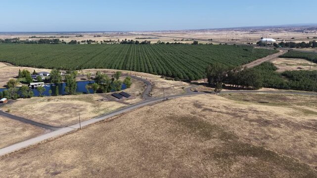 Aerial view of an expansive California farm landscape with dry golden fields, a green orchard, and a scenic rural pond estate