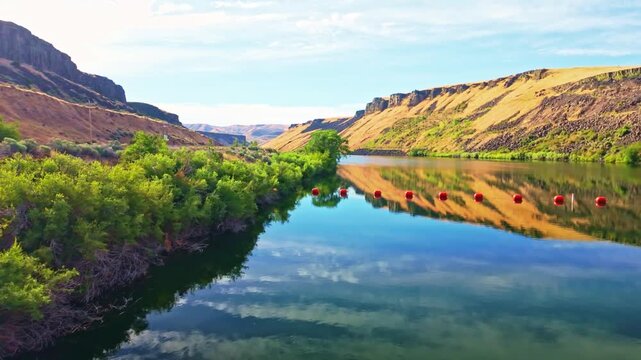Calm Boise River reflects golden basalt canyon cliffs with orange safety buoys along the water