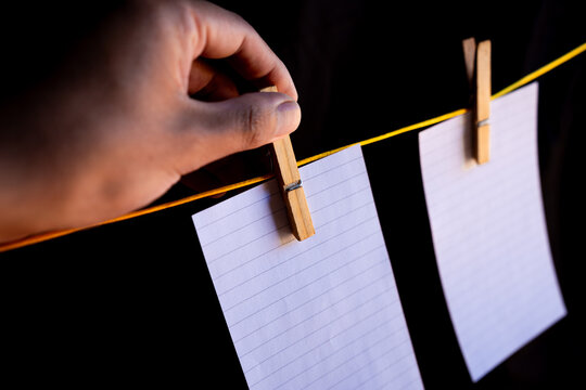 A hand hangs a blank note from a clothesline with a clothespin. Empty message card on a string, isolated on a black background