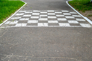 Obraz premium A black and white checkered finish line is painted across a cracked asphalt pathway on an outdoor children traffic training playground.