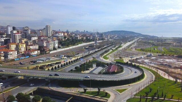 Aerial drone view of a newly constructed multi-level interchange on Maltepe coastal road with light vehicle traffic, residential buildings, green areas and partly cloudy spring sky, Istanbul, Turkey