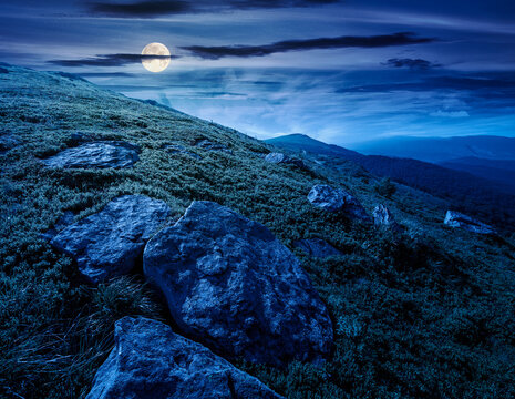 alpine meadow in summer nature at night. full moon over wild grass and grey rocks in carpathian landscape. mountain scenery of perechyn district, ukraine. mysterious fantasy