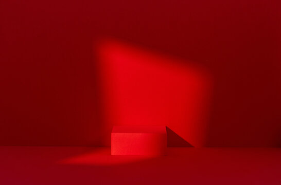 Minimal red monochrome studio scene with a cube pedestal and triangular geometric prop under a diagonal light beam, designed for product placement and commercial mockup use.