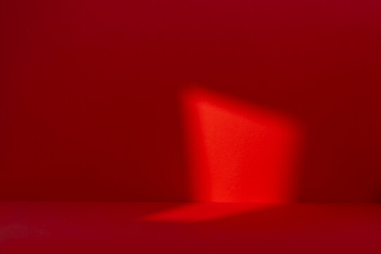 Abstract red studio scene featuring a diagonal beam of light and shadow on a dark red wall and floor, suitable for product placement and advertising backdrops.