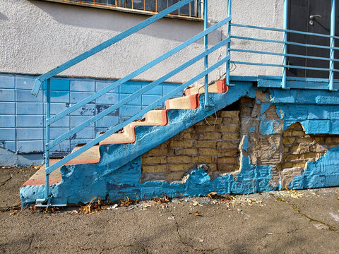 The school facade is deteriorating with missing tiles and broken steps
