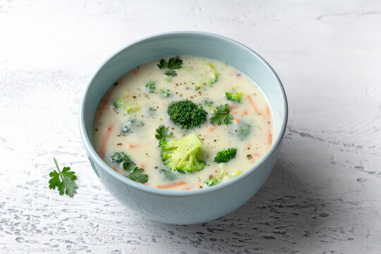 Creamy broccoli soup with potatoes, carrots and herbs in a blue bowl. Homemade vegetable soup with a rich texture on a light background