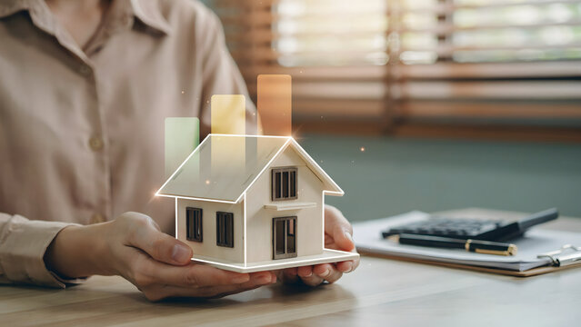 Hands holding a small wooden house model with glowing bar chart representing real estate market growth and property investment analysis