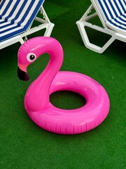 Bright pink inflatable flamingo pool float on a green grass lawn near sunbeds at a summer resort. © photon_photo