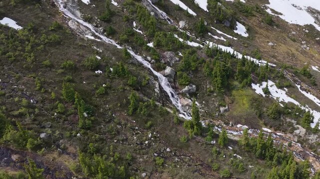 Stunning Waterfall Cascading Down a Verdant Mountain Slope with Patches of Snow in British Columbia, Canada