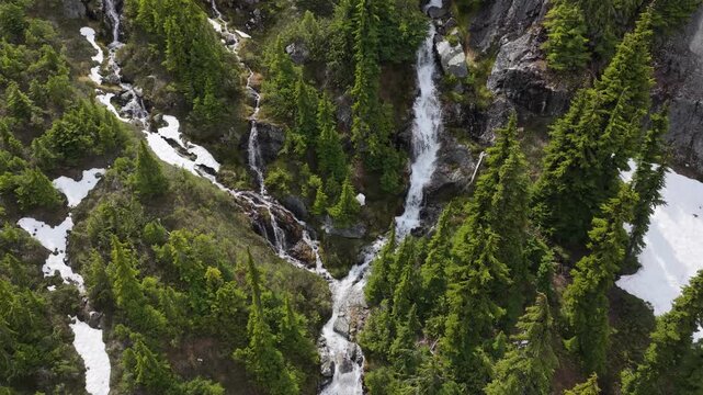 Cascading Mountain Waterfalls Amidst Lush Green Forest and Snow Patches in British Columbia, Canada
