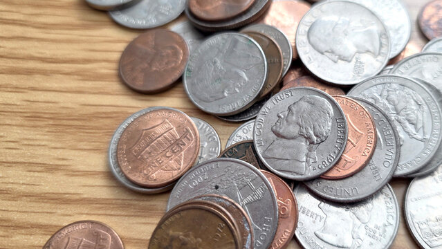 collection of united states USD nickels, pennies, quarters and dime coins scattered on a wood surface