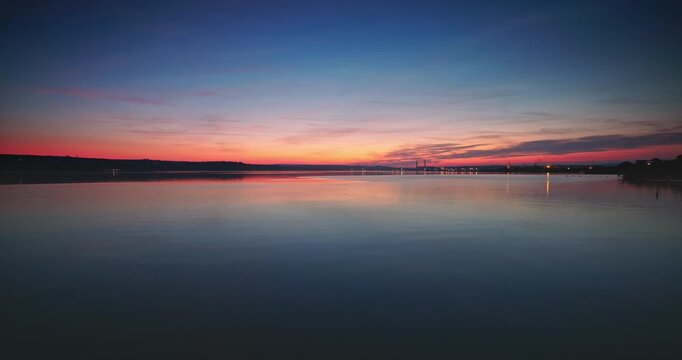 Colorful sunset sky reflecting on calm lake water with distant city lights