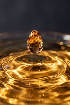 Macro shot of a golden amber liquid drop suspended over circular ripples on a dark background