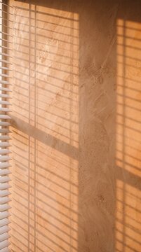 Warm sunlight casting geometric shadows of window blinds onto a textured orange plaster wall