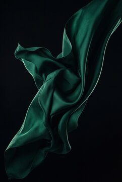 Elegant emerald green silk fabric flowing and waving against a solid black background