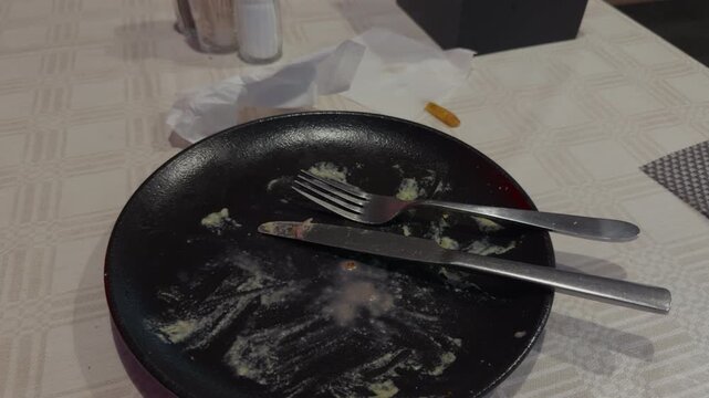 Dirty empty dinner plate with fork and knife resting on table after meal in casual dining setting