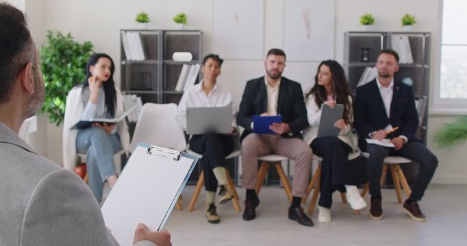 Group of multiethnic business people engaged in professional briefing led by corporate male trainer answer questions, conduct corporate seminar for staff members gathered together in modern office