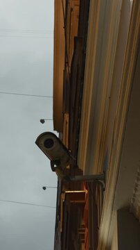 Security camera mounted on building exterior watching urban street from low angle beside old facade at dusk