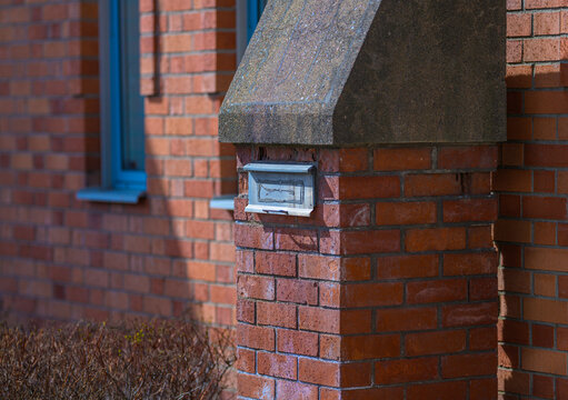 Close up of red brick wall with mounted mailbox and architectural detail in sunlight.