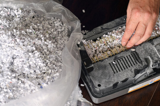 Close-up high angle shot showing hand removing stuck shredded paper from shredder blades next to bag of waste