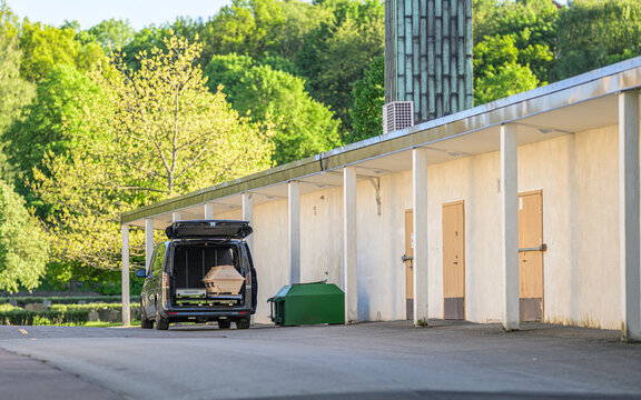 Funeral vehicle with coffin outside crematorium building in greenery.