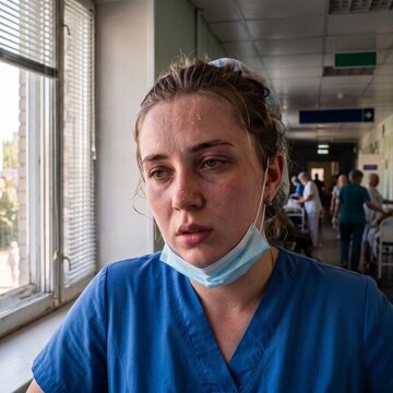 Exhausted and sweating nurse in a hospital corridor. Overworked female healthcare worker with face mask pulled down looking stressed