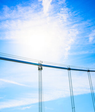 Bridge maintenance crew silhouetted beneath bright sun and cables.
